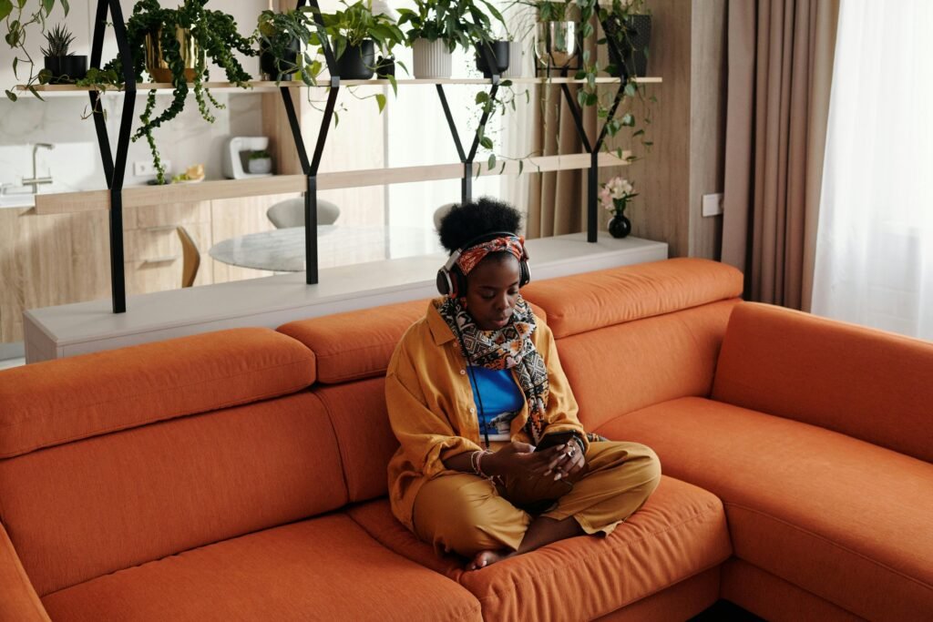 pexels photo 5711711 5711711 A woman enjoys music with headphones while relaxing on an orange sofa.